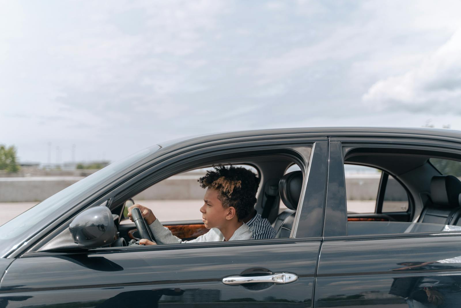 Side view of a young male teenager focused on driving a car in bright daylight.